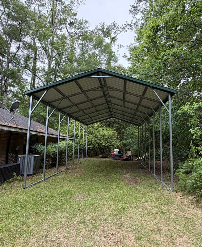 Open-sided metal carport with green roof nestled among trees in a wooded backyard