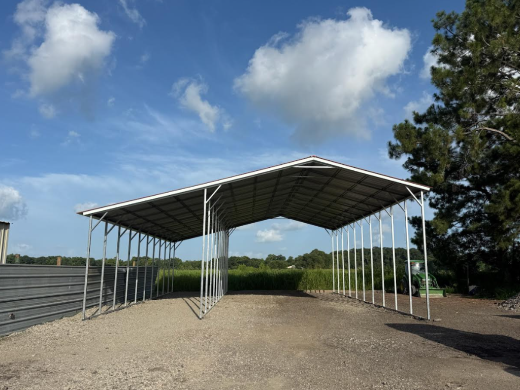 White and gray gable-roof carport on a gravel pad under a blue sky