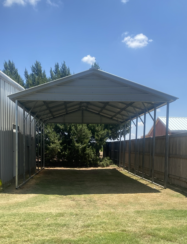 White metal carport with gable roof nestled among pine trees in a backyard