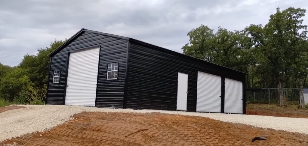 Black metal barn-style garage with white trim, roll-up doors, and windows