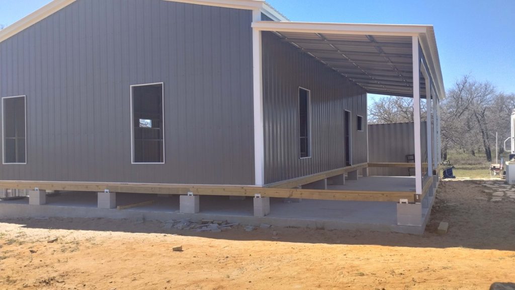 Gray metal building under construction with covered porch and deck framing