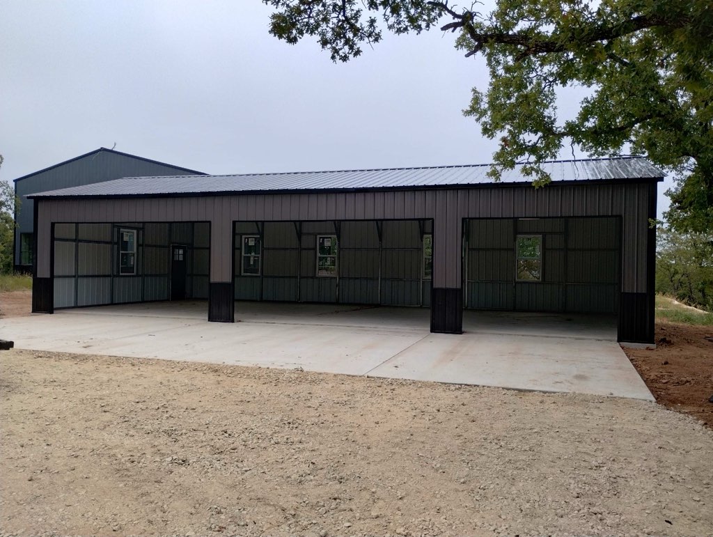 Large gray metal building with three open bays and windows, on gravel